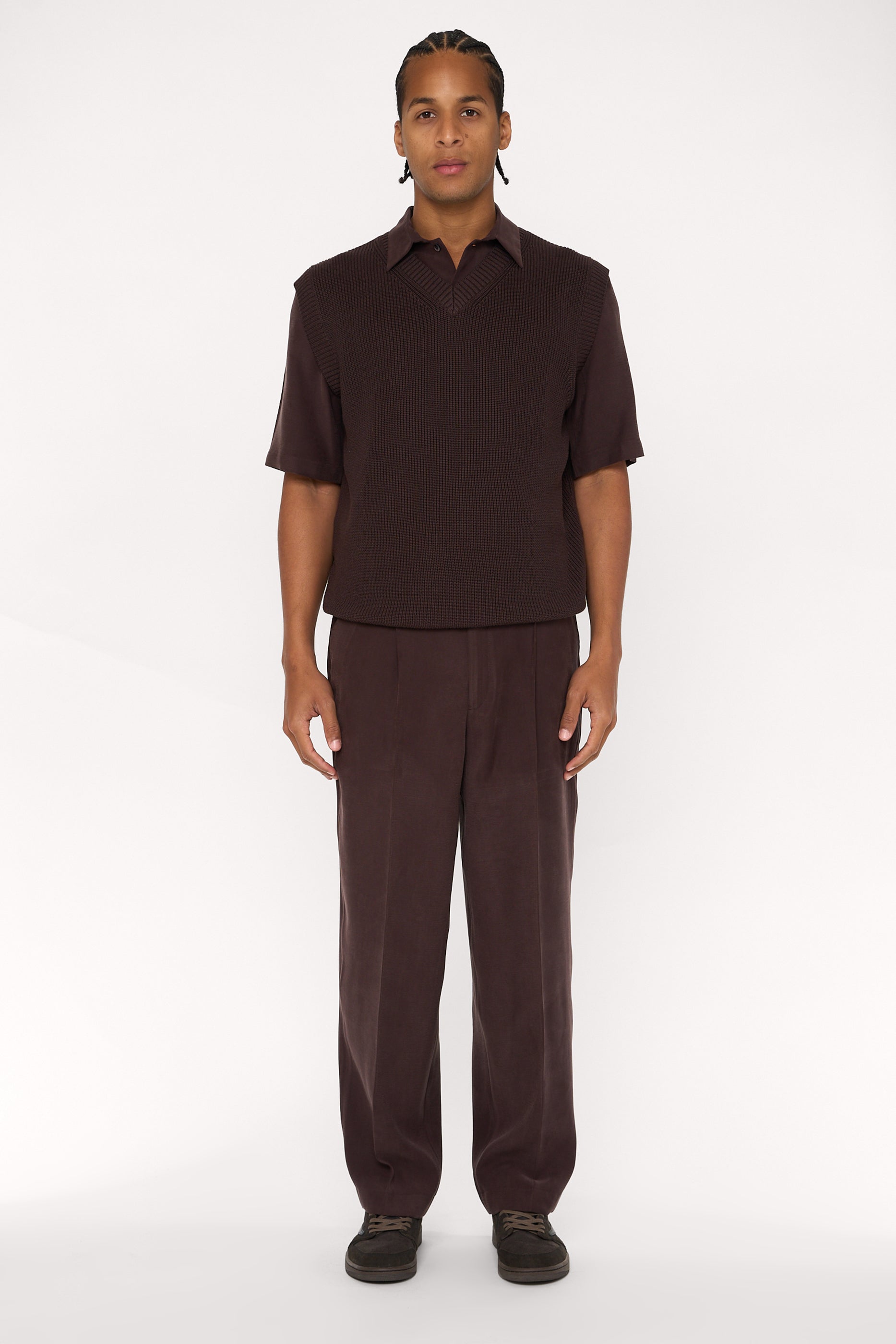 Maroon brown cotton and lyocell knit vest with a relaxed fit, worn over a brown relaxed shirt and wide pleated trousers.