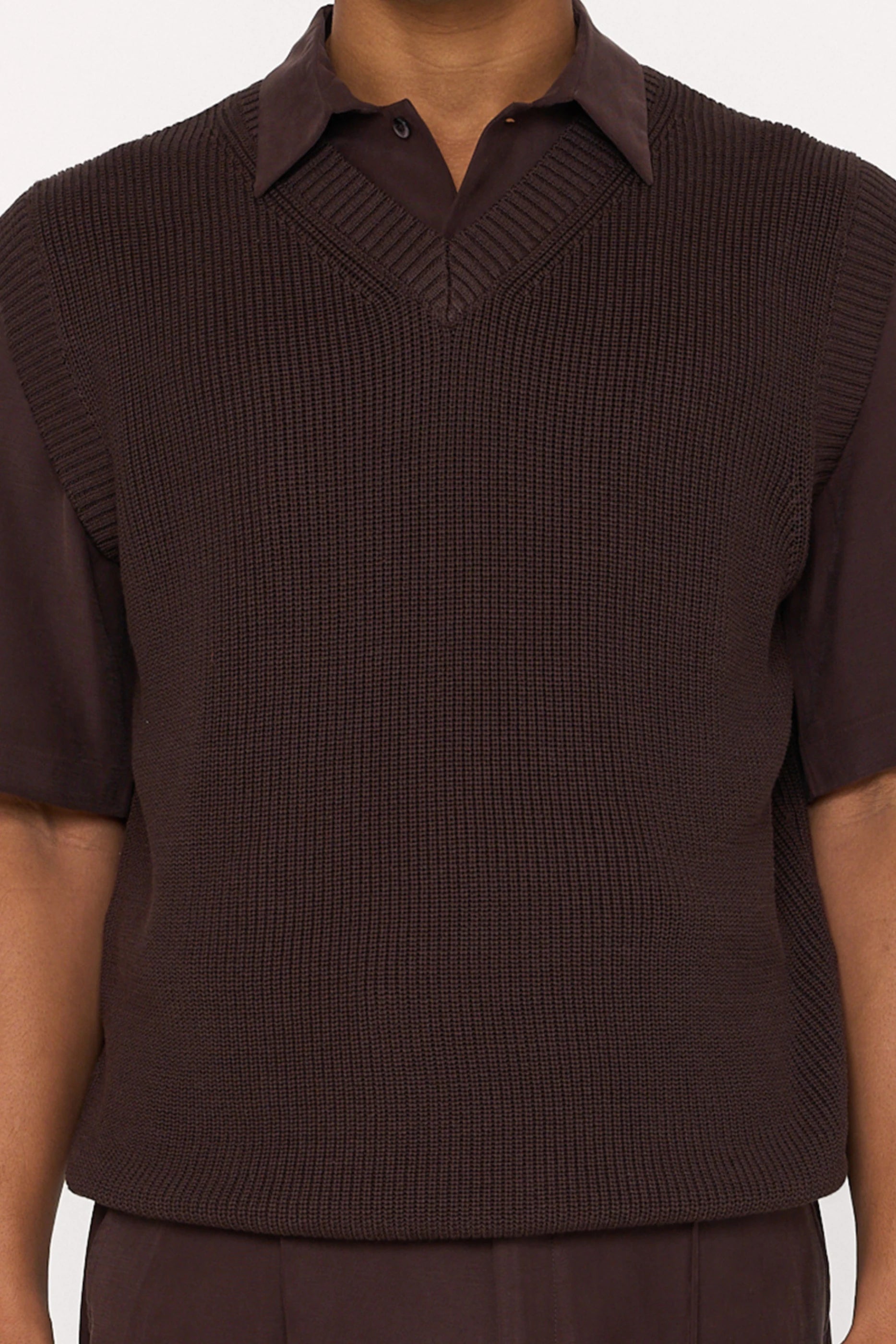 Close up of a maroon brown cotton and lyocell knit vest with a relaxed fit, worn over a brown relaxed shirt.