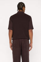 Back view of a maroon brown cotton and lyocell knit vest with a relaxed fit, worn over a brown relaxed shirt.