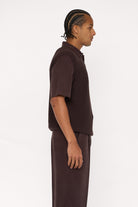 Side view of a maroon brown cotton and lyocell knit vest with a relaxed fit, worn over a brown relaxed shirt.